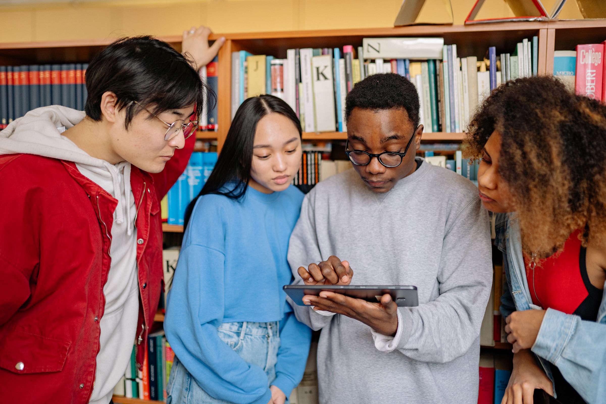 Four students gathered around a tablet in the school library.