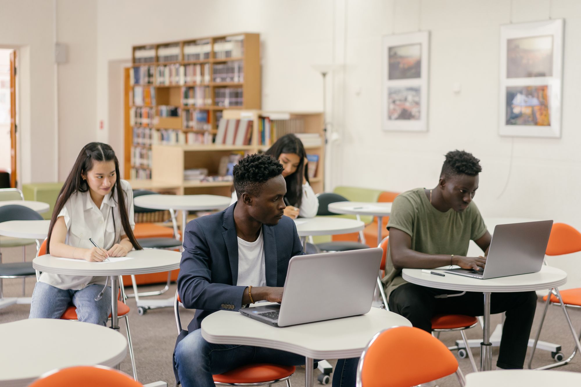 Students working on laptops and notes in a bright, modern study room.