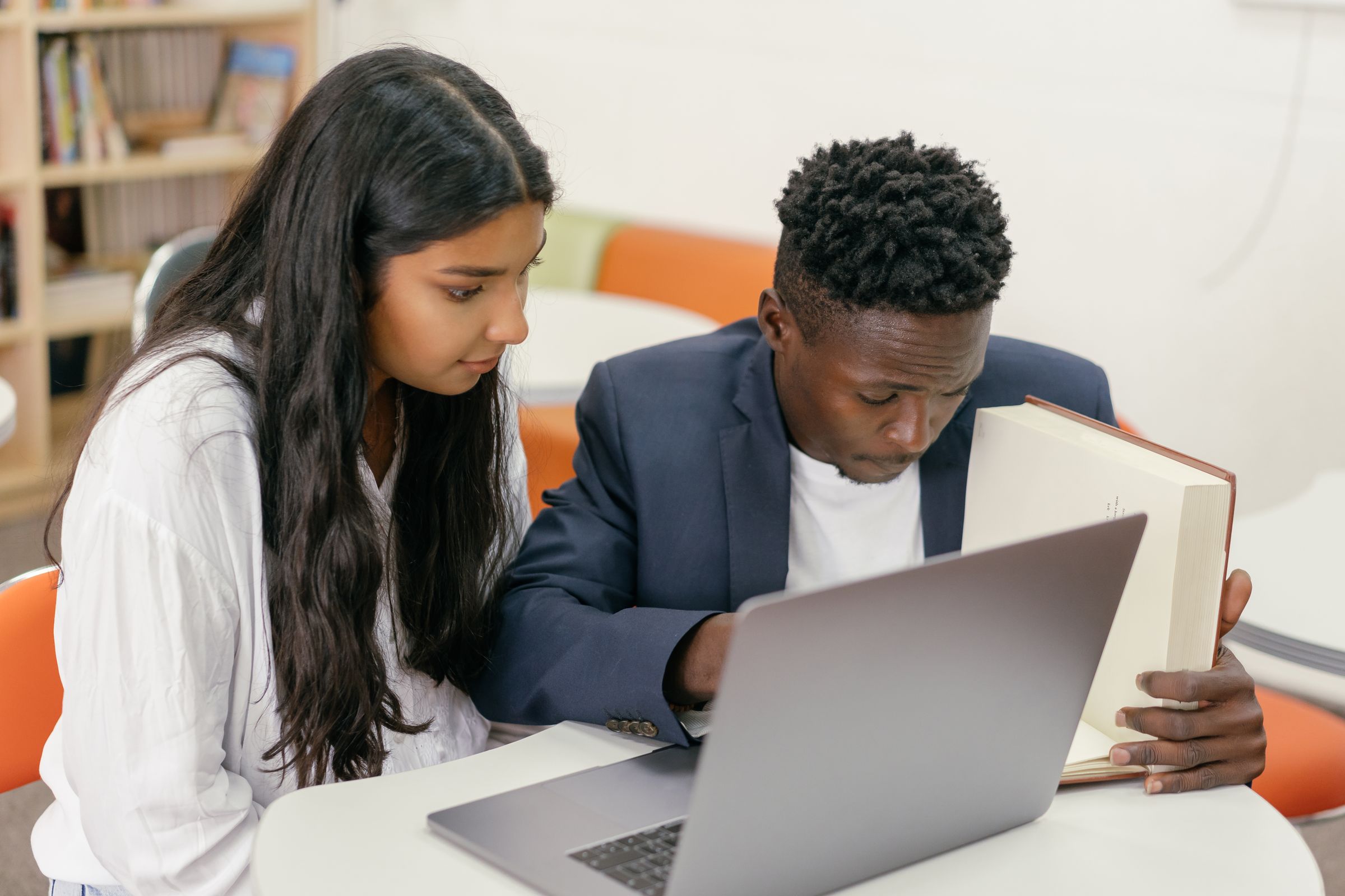 A student in a blazer working on a laptop beside a classmate.